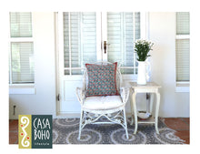 Load image into Gallery viewer, White wicker chair with a patterned cushion in a bright room with large windows.
