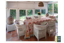 Load image into Gallery viewer, Dining area with wicker chairs and a floral tablecloth in a sunroom.
